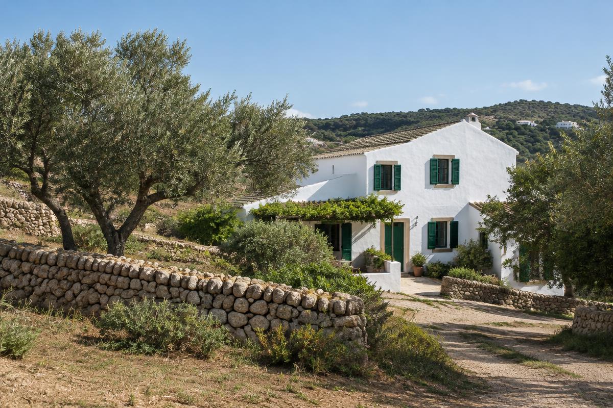 Whitewashed Menorcan farmhouse with green shutters among olive trees and dry-stone walls near Es Mercadal; illustrative, not a photograph of the listed property