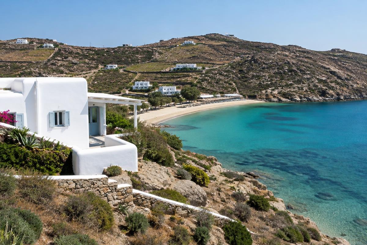 Cycladic house above the sheltered sandy bay of Psarou, Mykonos; illustrative, not a photograph of the listed property